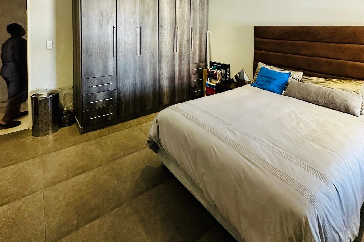 A well-maintained bedroom featuring large built-in cupboards, neutral tiled flooring, and recessed ceiling lighting.