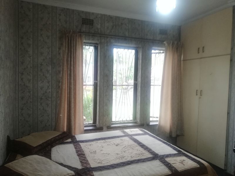 A bedroom featuring built-in cupboards, security bars on the windows, and dated wallpaper finishes.