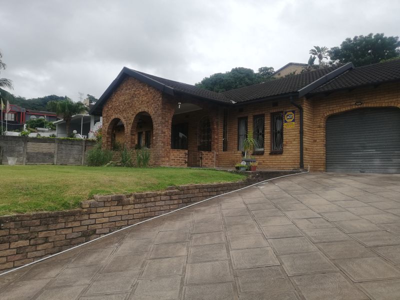 Front elevation of a face brick house featuring an arched covered porch, paved driveway, and a secure roller shutter garage door.