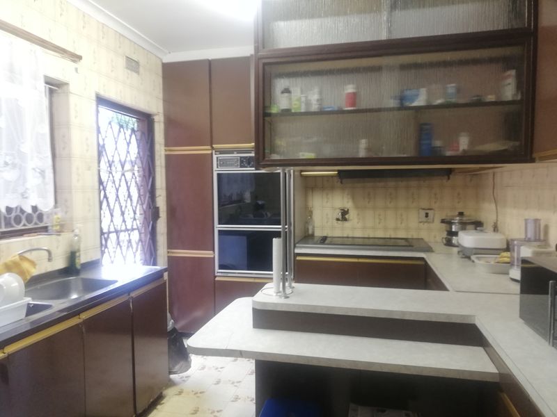 A dated kitchen featuring built-in oven, hob, laminate countertops, and ample cabinetry, offering significant potential for a modern renovation.