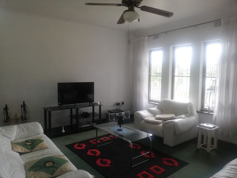 A living room featuring carpet flooring, a ceiling fan, and large windows fitted with security bars.