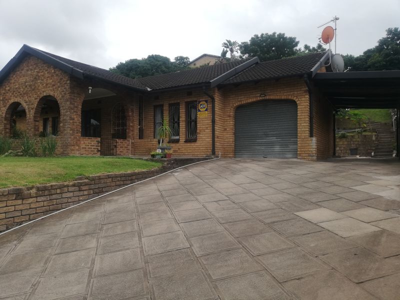 Front elevation of a face brick house featuring an arched porch, a roller shutter garage, a paved driveway, and an attached carport.