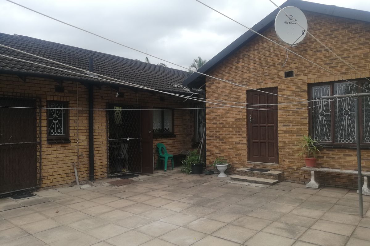 A rear exterior view of a face brick house featuring a paved patio area, security gates, and a tiled roof.