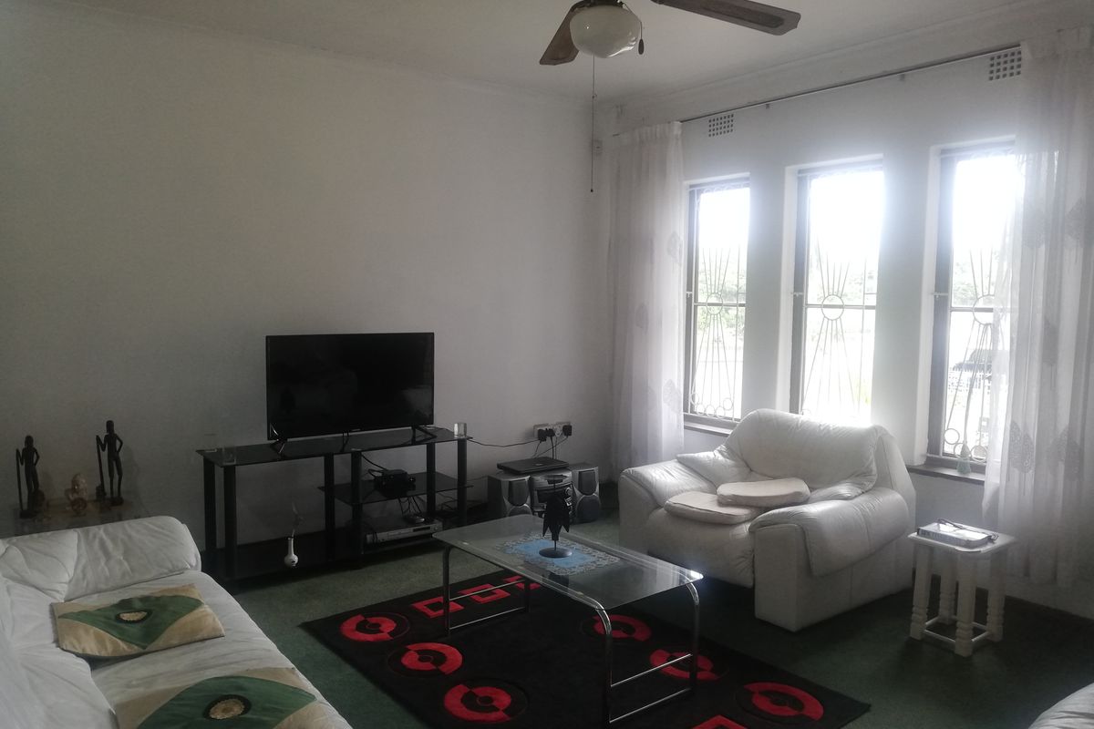 A living room featuring carpet flooring, a ceiling fan, and large windows fitted with security bars.