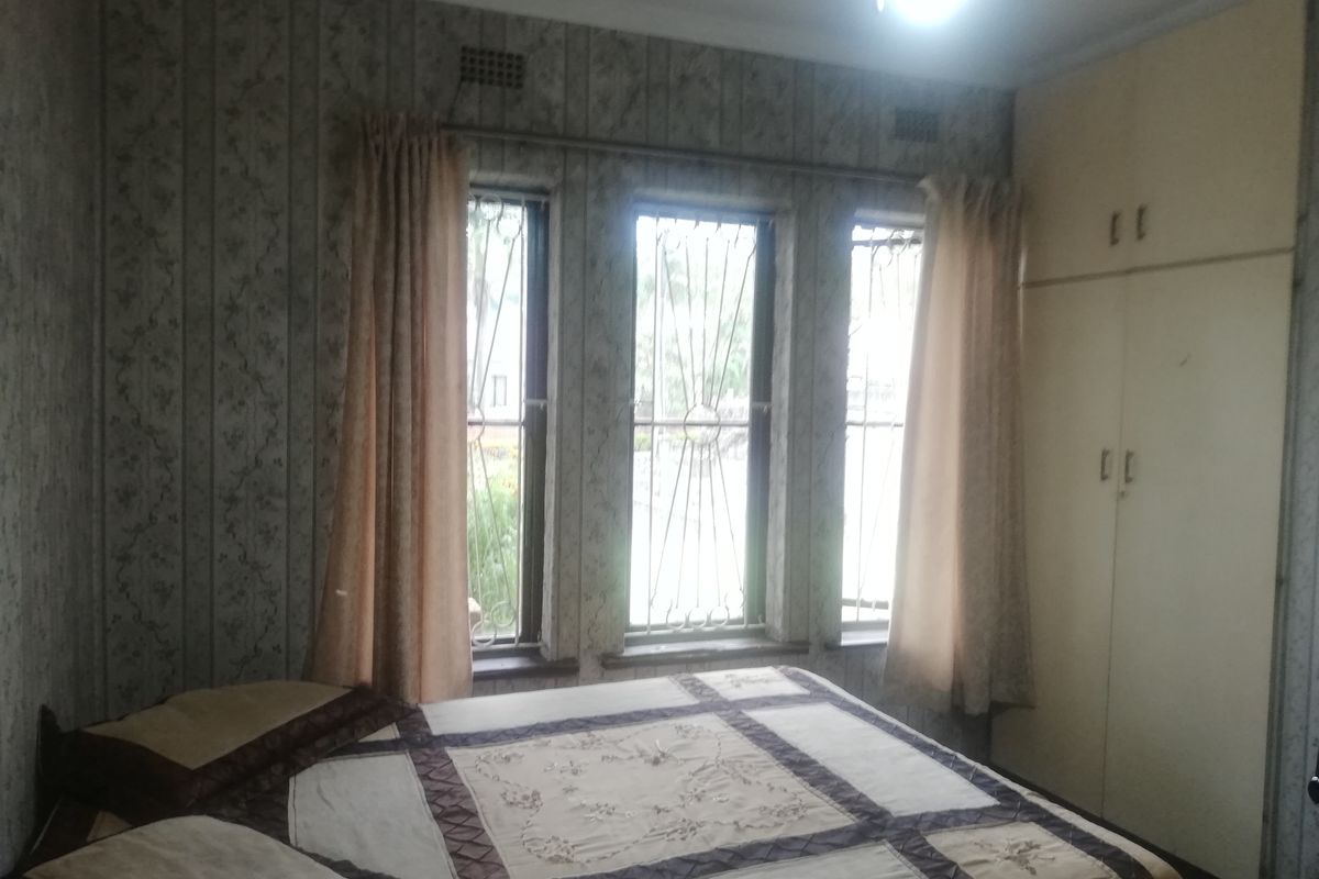 A bedroom featuring built-in cupboards, security bars on the windows, and dated wallpaper finishes.