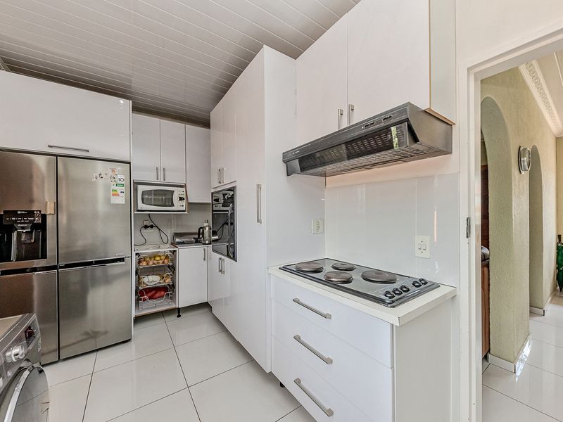 A functional kitchen featuring white cabinetry, built-in oven, electric hob with extractor fan, and tiled flooring, providing a clean and practical workspace.