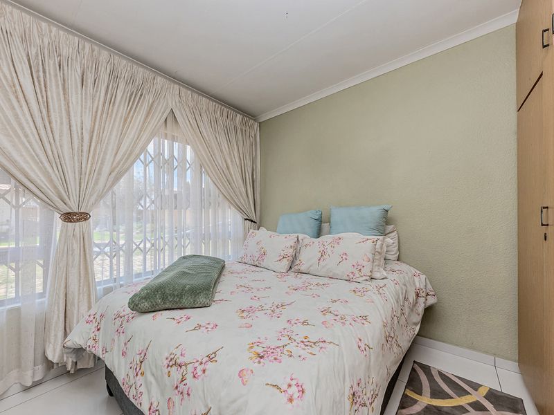 A functional bedroom featuring built-in wardrobes, tiled flooring, and a security gate on the window, offering a clean and practical living space.
