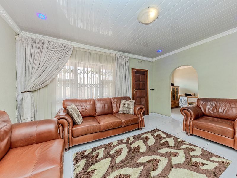 A living room featuring tiled flooring, arched architectural details, and glossy ceiling panels with integrated lighting, providing a functional and connected living space.