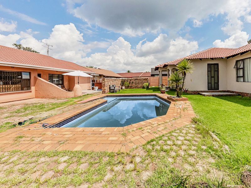Rear garden area featuring a swimming pool with brick surround, lawn, and surrounding residential structures with tiled roofs.