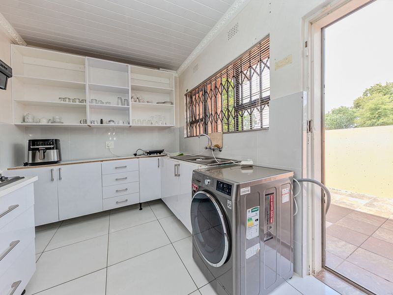 Functional scullery area featuring white cabinetry, tiled flooring, stainless steel sink, and direct access to the outdoor patio area.