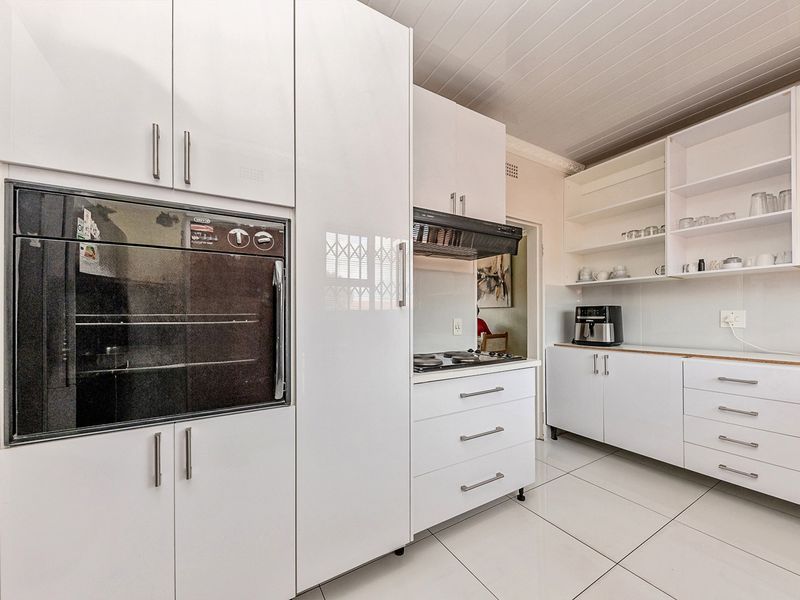 A clean, modern kitchen featuring white cabinetry, built-in oven, gas hob with extractor fan, and tiled flooring.
