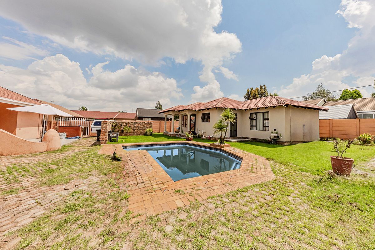 Rear exterior view featuring a swimming pool, brick-paved surround, lawn, and boundary wall, set against the back facade of the house.