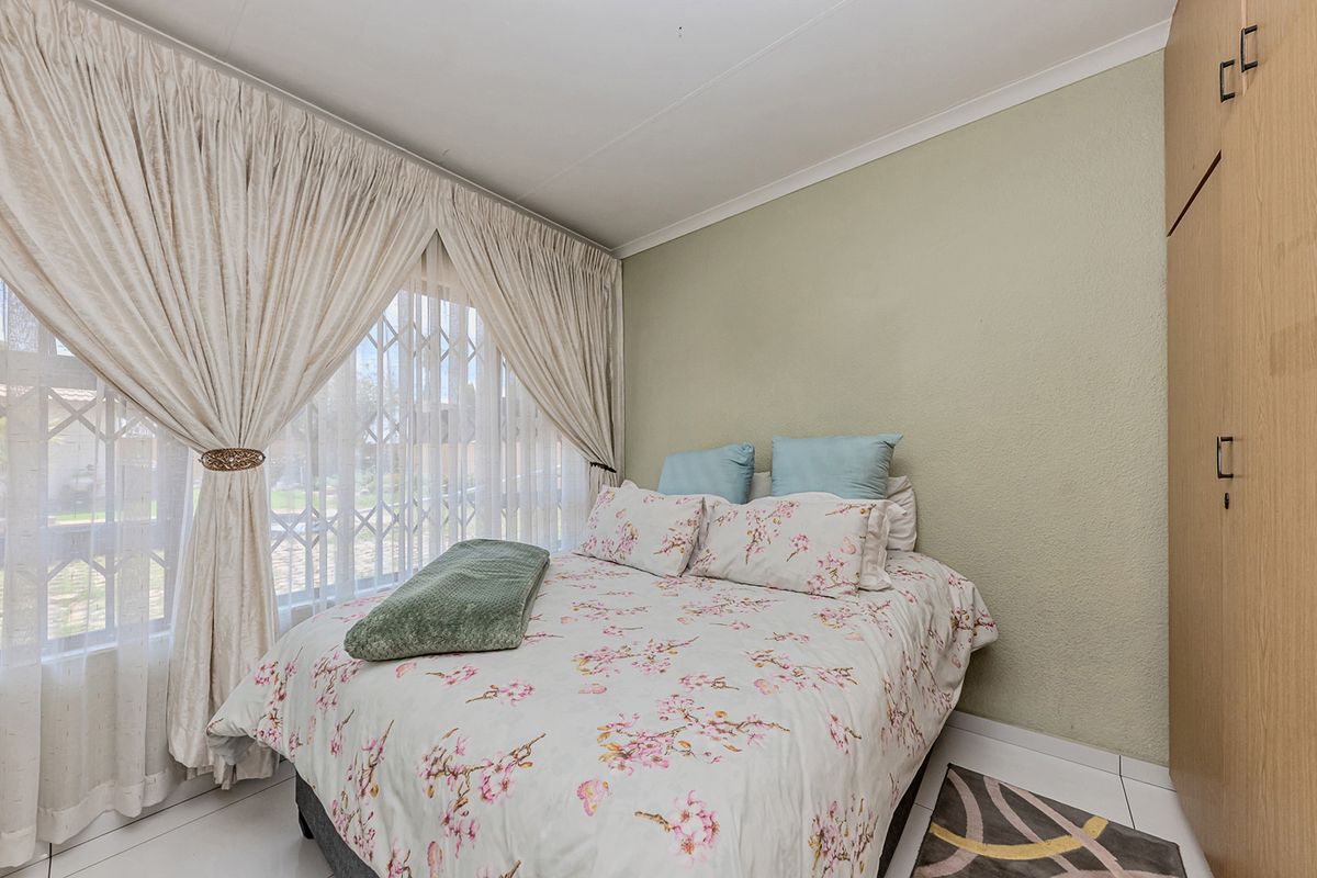 A functional bedroom featuring built-in wardrobes, tiled flooring, and a security gate on the window, offering a clean and practical living space.