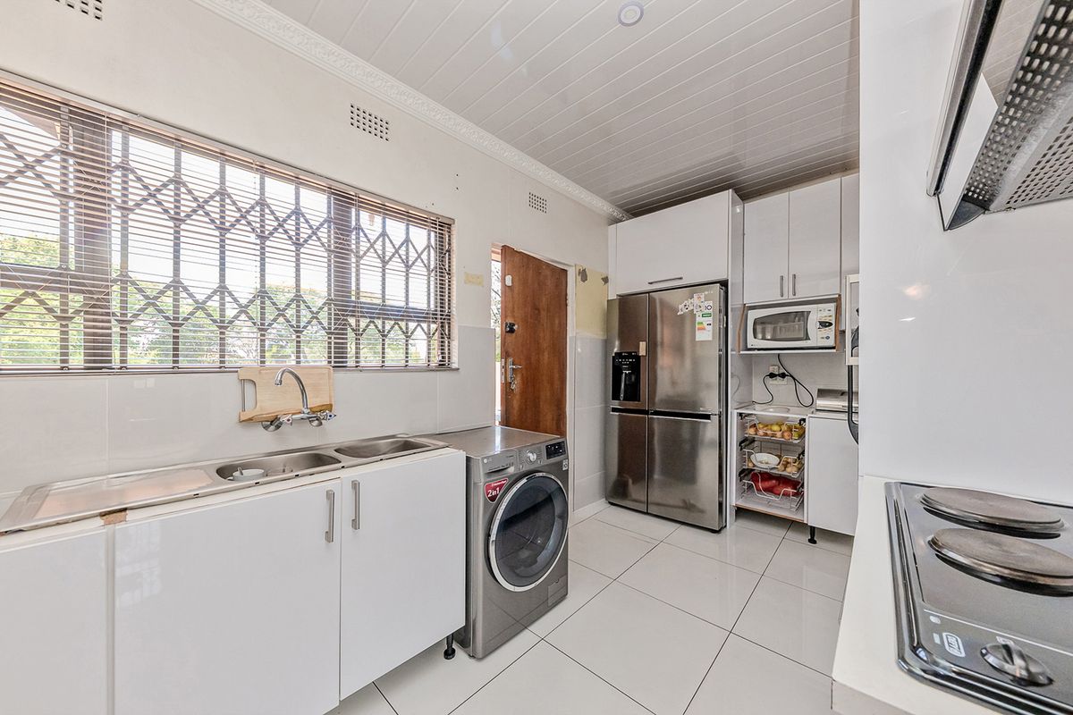 A functional kitchen featuring white cabinetry, tiled flooring, a stainless steel sink, and integrated appliances, with a security gate on the window.