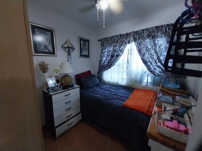 A compact bedroom featuring tiled flooring and a ceiling fan, providing a functional space for rest.