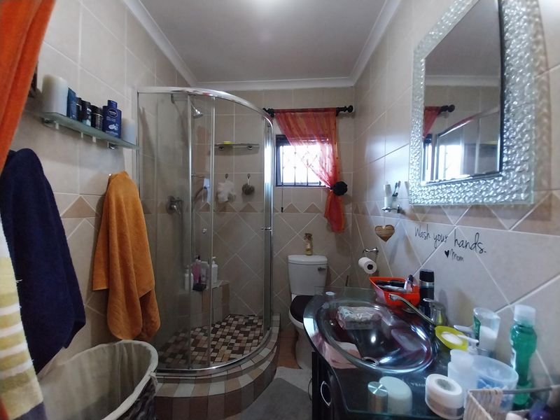 A functional bathroom featuring a curved glass shower enclosure, tiled walls, a vanity basin, and a toilet.