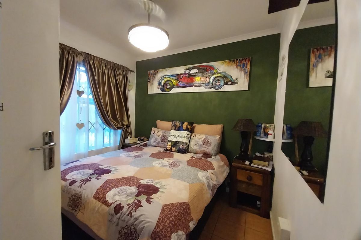 A cozy bedroom featuring tiled flooring, a feature wall, and a window fitted with security bars.