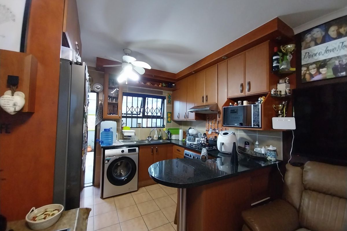 Compact kitchen featuring wooden cabinetry, granite countertops, integrated appliances, and tiled flooring, with direct access to an outdoor area.