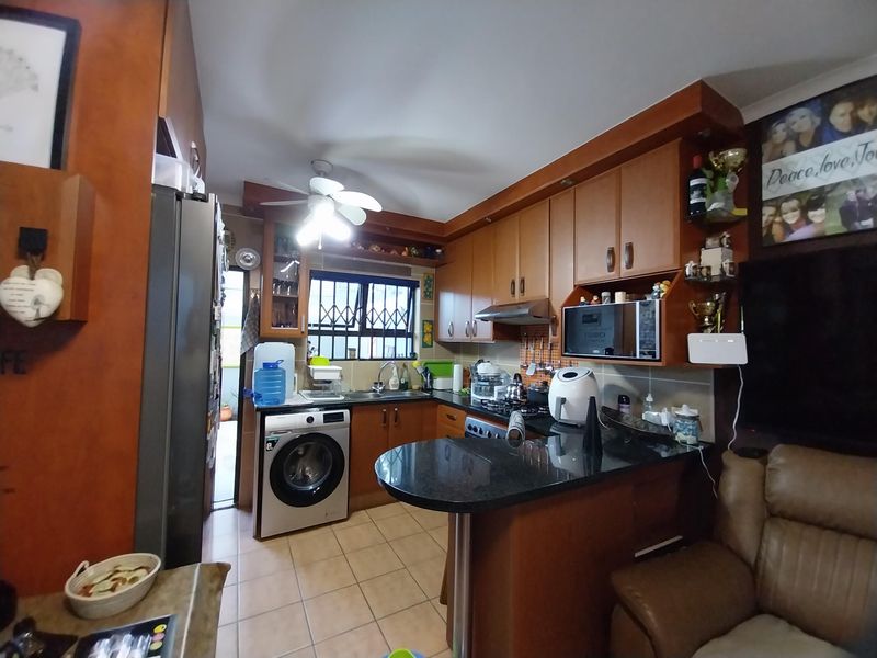 Compact kitchen featuring wooden cabinetry, granite countertops, integrated appliances, and tiled flooring, with direct access to an outdoor area.