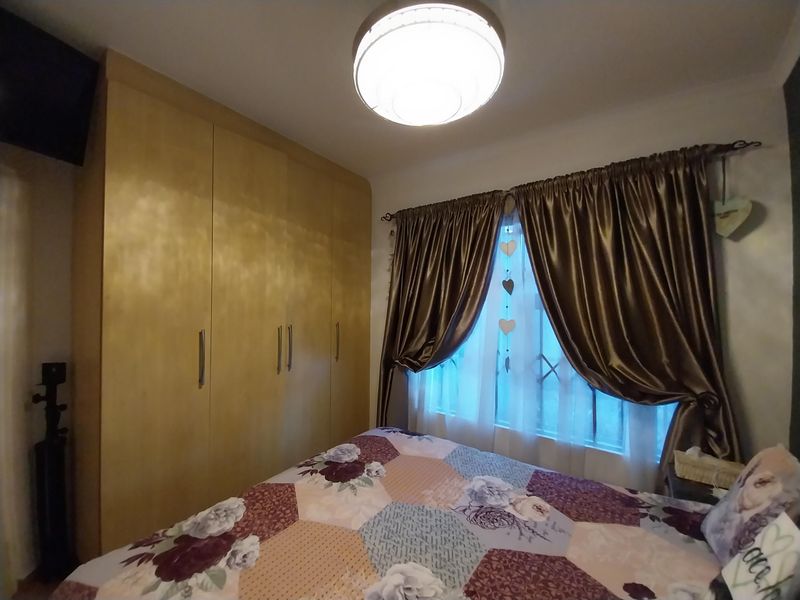 A cozy bedroom featuring built-in wooden cupboards and a window fitted with security bars, providing functional storage and natural light.