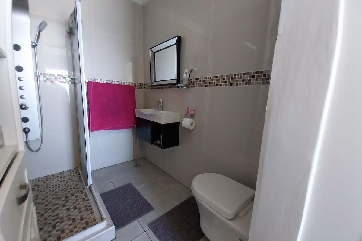A modern bathroom featuring a glass-enclosed shower with a multi-jet shower panel, a wall-mounted vanity with basin, and a toilet.