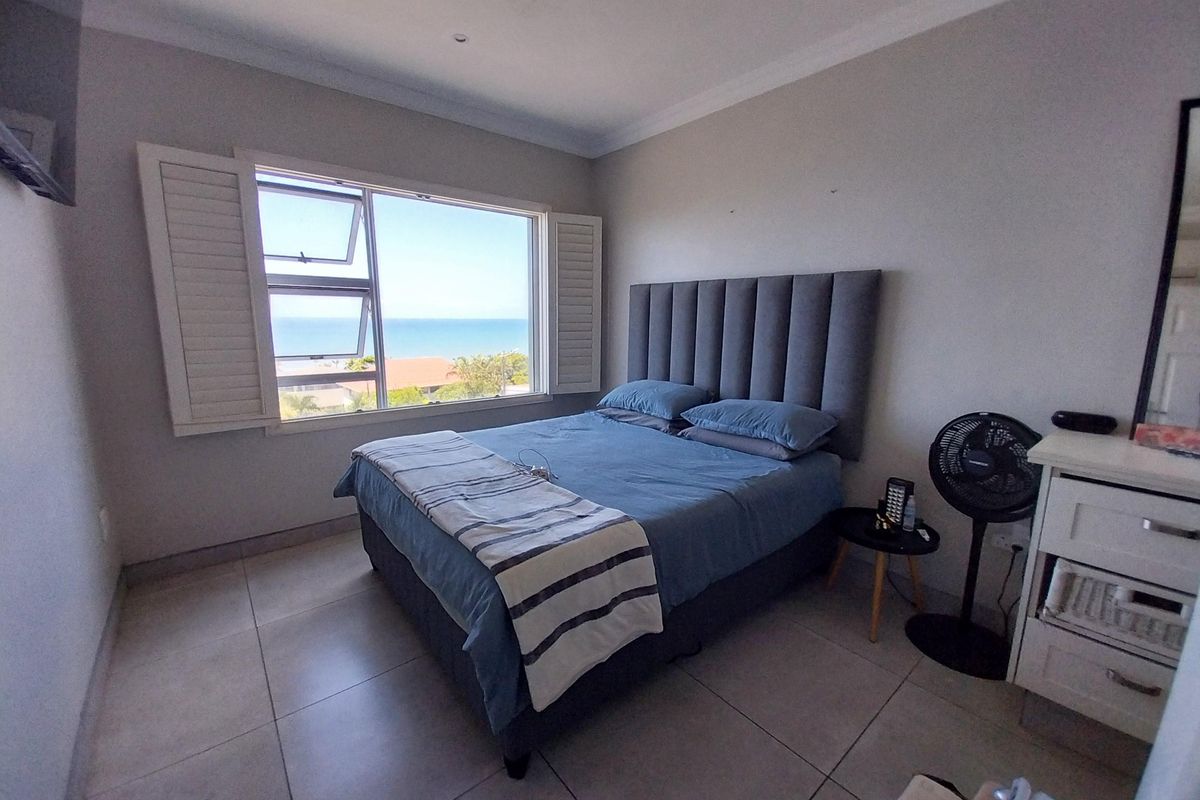 A bright bedroom featuring large windows with plantation shutters, tiled flooring, and a scenic ocean view.