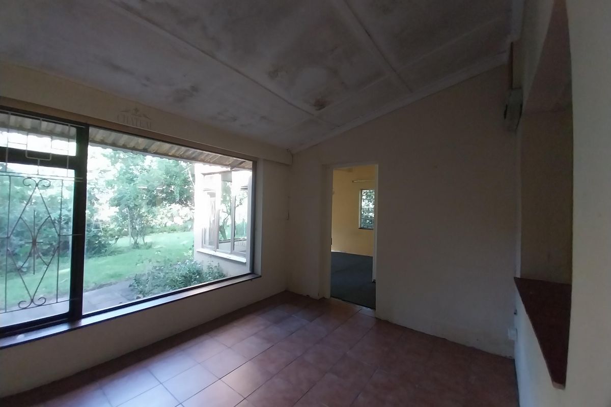 An empty living area featuring large windows with security bars, tiled flooring, and a ceiling showing signs of significant water staining or wear.