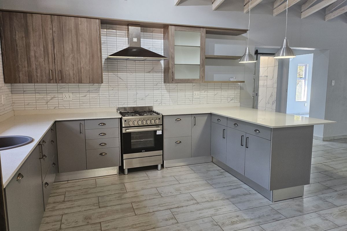 Modern kitchen featuring grey cabinetry, stone countertops, gas stove with extractor, tiled backsplash, and exposed timber ceiling beams in an open-plan layout.