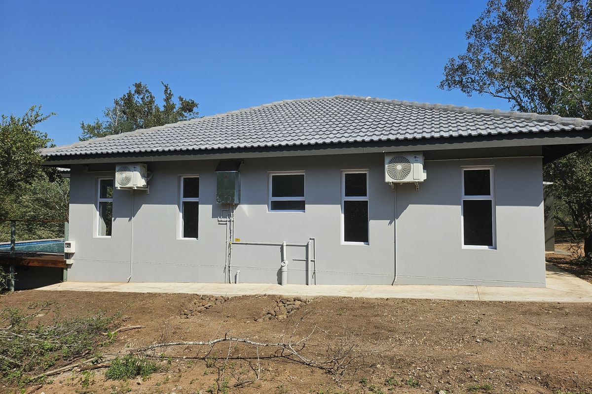 Rear elevation of a modern house featuring a tiled roof, grey rendered walls, and multiple air conditioning units installed.