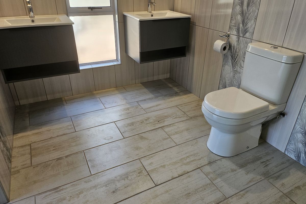 Modern bathroom featuring dual wall-mounted vanities with ceramic basins, chrome fixtures, and contemporary tiled finishes throughout.
