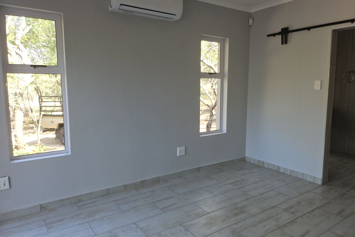 A bright, empty bedroom featuring modern tiled flooring, aluminium windows, and a wall-mounted split-system air conditioner.