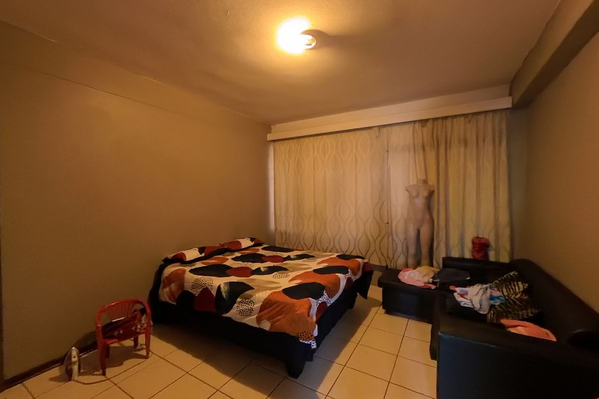 A bedroom featuring tiled flooring and large window curtains, providing a functional living space.
