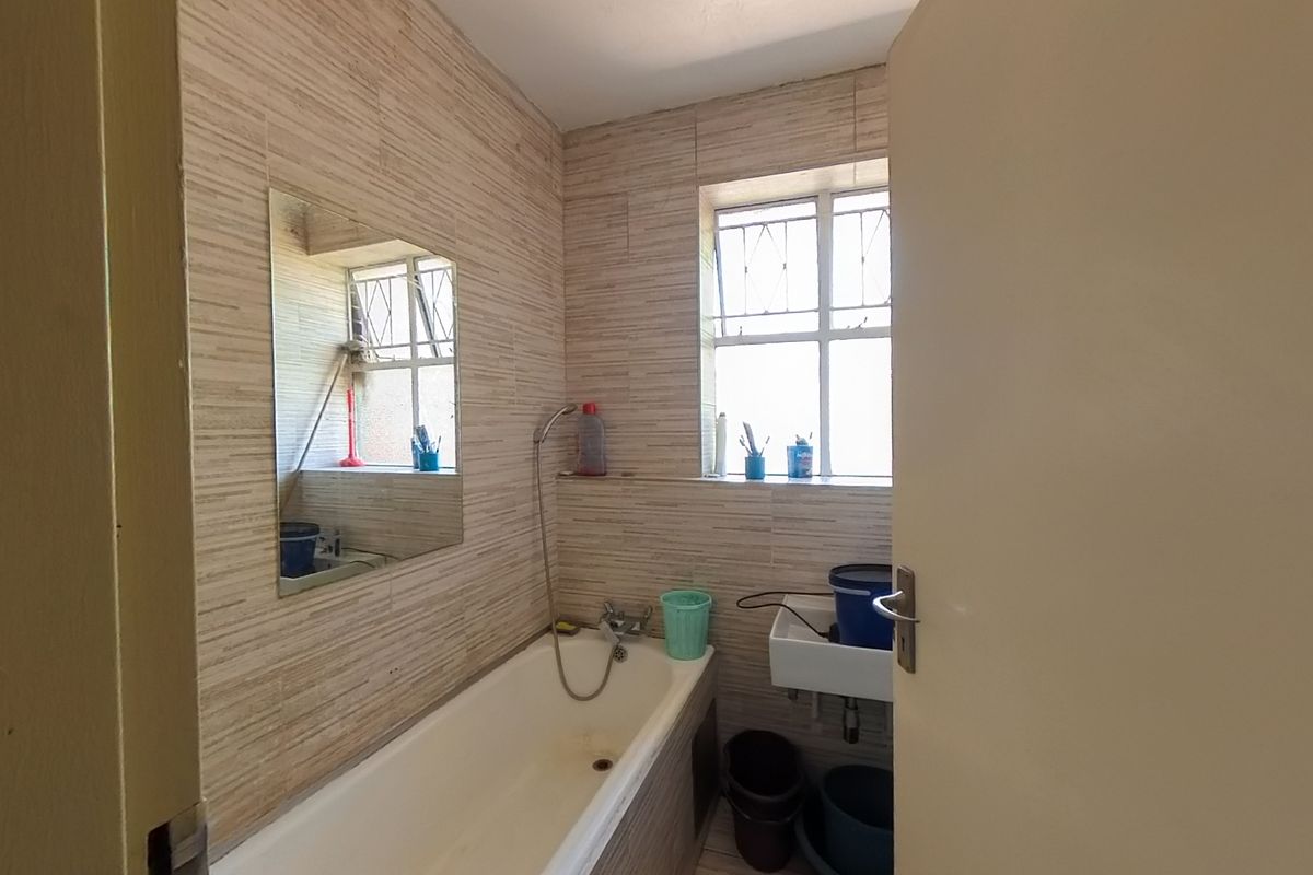 A compact bathroom featuring a bathtub with a handheld shower attachment, a wall-mounted basin, and tiled walls.