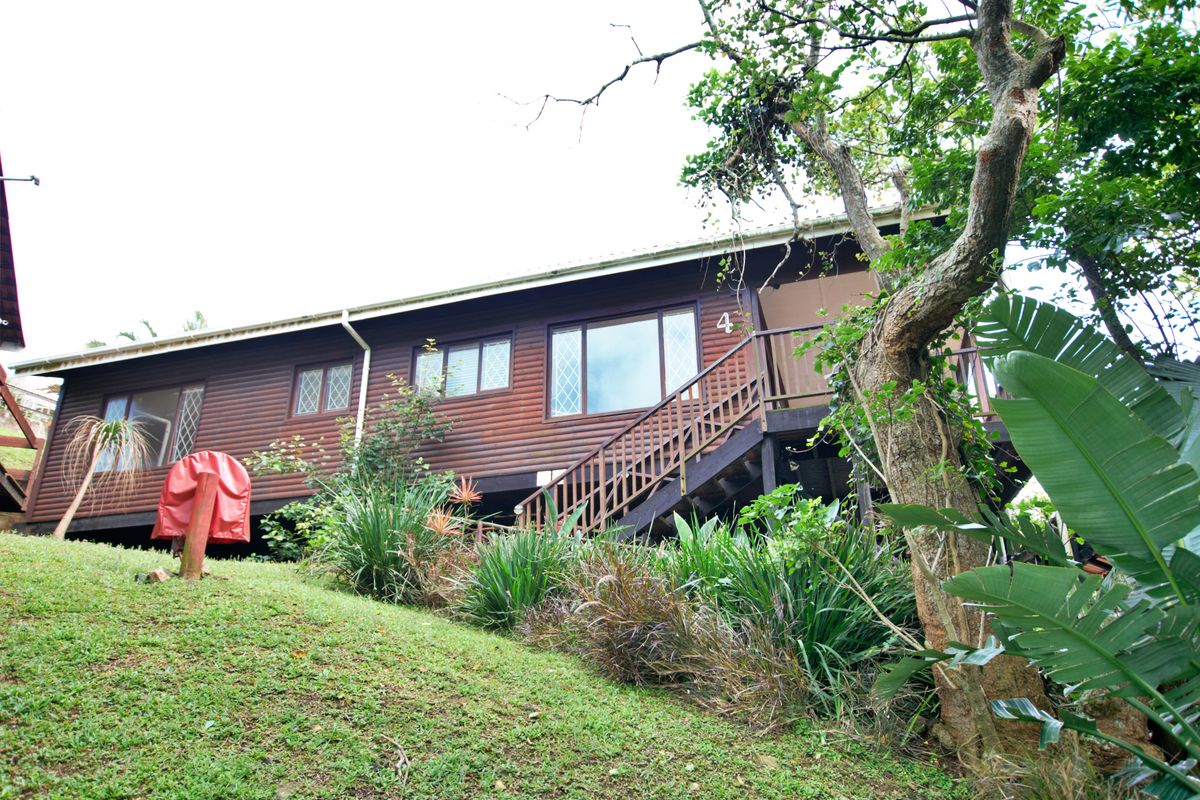 A view of the exterior rear of the townhouse, featuring timber cladding, elevated wooden staircase, and a sloped garden area.
