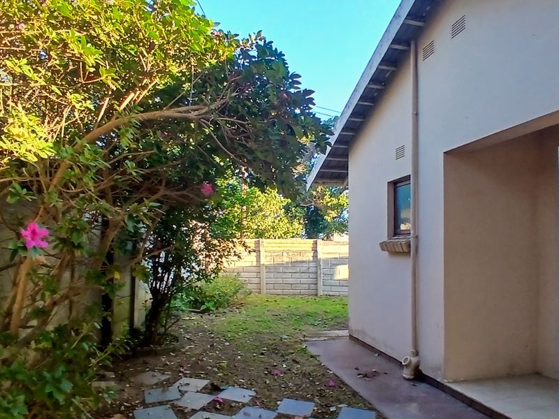 Rear exterior view of the property featuring a paved walkway, security gate, and a concrete block boundary wall with surrounding garden area.