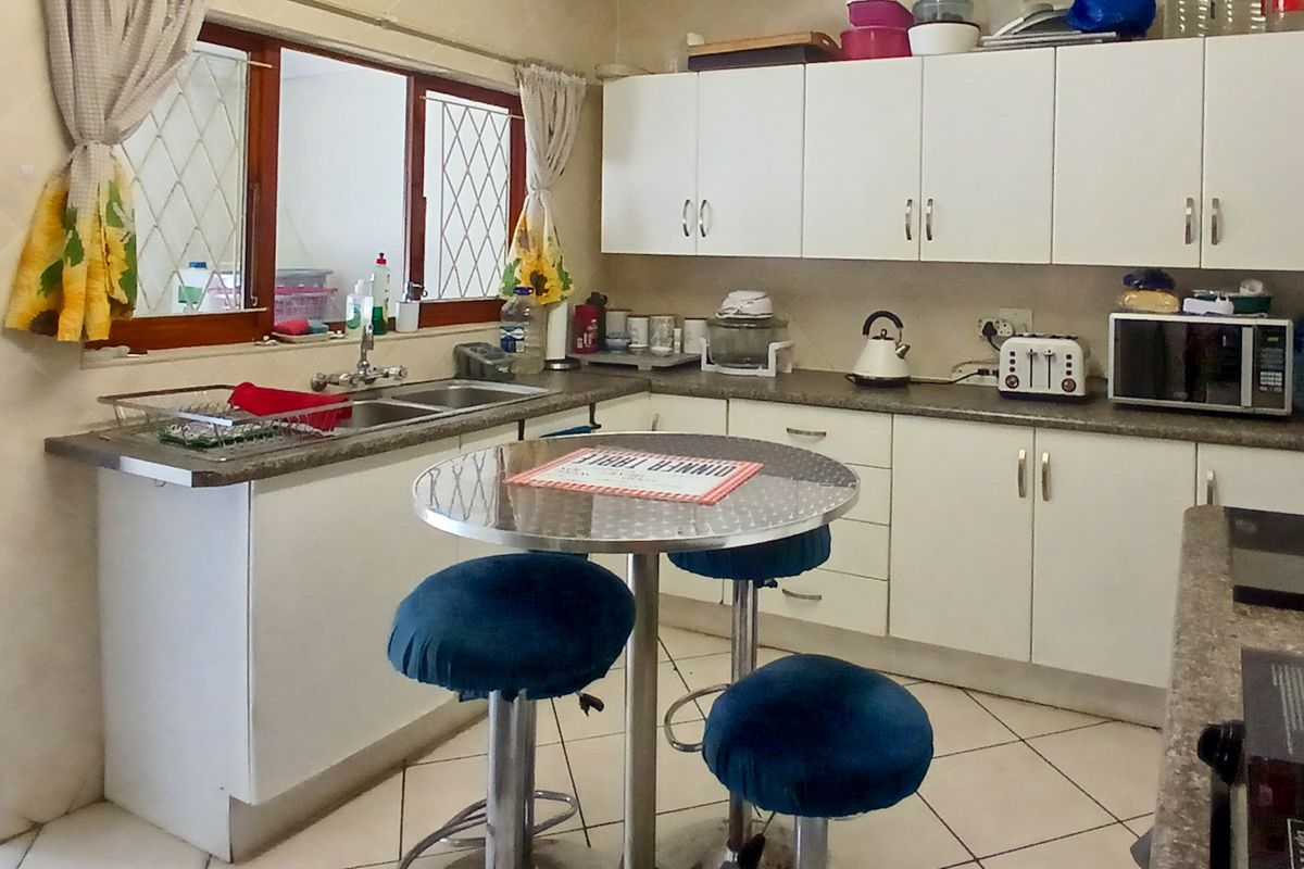 A functional kitchen featuring white cabinetry, laminate countertops, a double bowl sink, and tiled flooring with security bars on the windows.