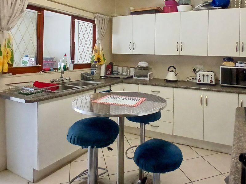 A functional kitchen featuring white cabinetry, laminate countertops, a double bowl sink, and tiled flooring with security bars on the windows.