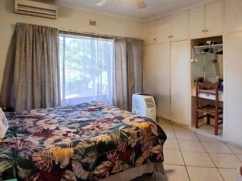 A bedroom featuring tiled flooring, built-in cupboards with an integrated vanity area, and a wall-mounted air conditioning unit.