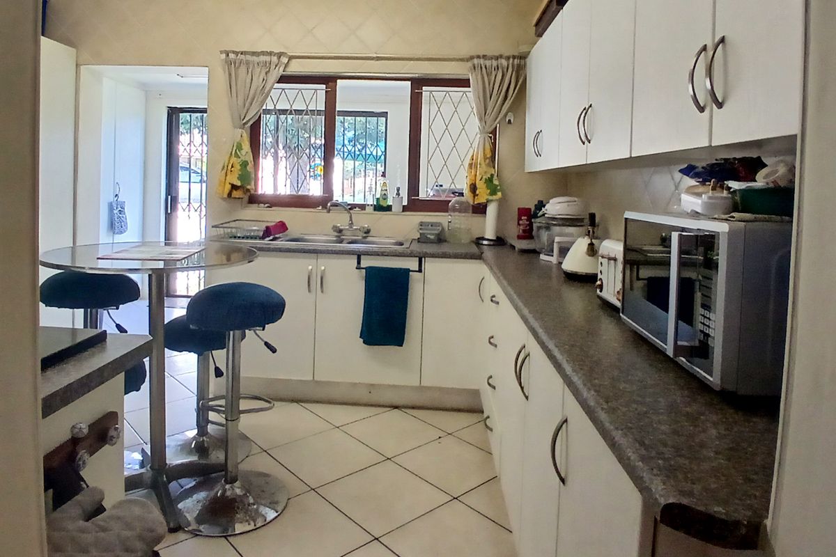 Functional kitchen featuring white built-in cabinetry, laminate countertops, double basin sink, and tiled flooring with security bars on the windows.