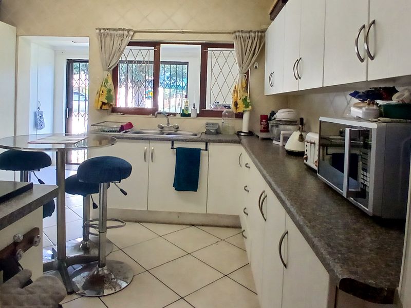 Functional kitchen featuring white built-in cabinetry, laminate countertops, double basin sink, and tiled flooring with security bars on the windows.