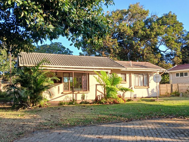 Front view of a single-story house featuring a tiled roof, security bars on windows, and a paved driveway set within a garden.