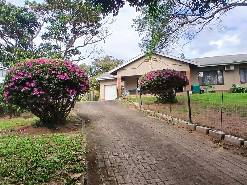 Front view of a single-story house featuring a paved driveway, attached garage, and established garden with mature landscaping.