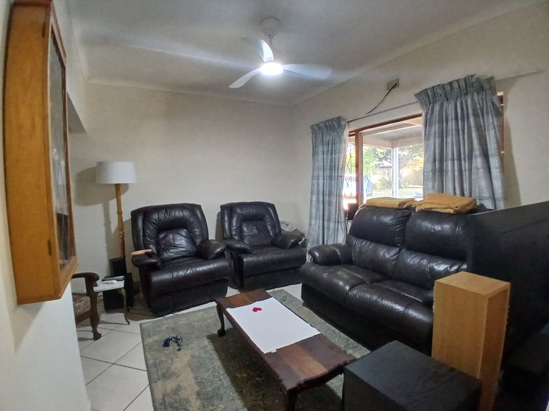 A functional living room featuring tiled flooring, a ceiling fan, and large windows with curtain rails, offering a comfortable and practical living space.