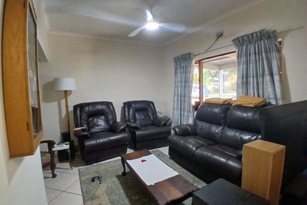A functional living room featuring tiled flooring, a ceiling fan, and large windows with curtain rails, offering a comfortable and practical living space.