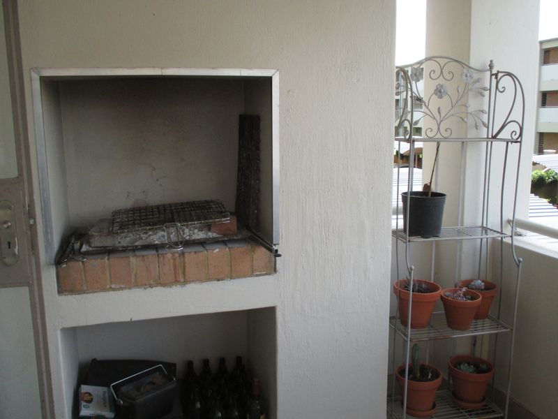 A covered balcony featuring a built-in brick braai area with a metal hearth, providing a functional outdoor entertainment space.