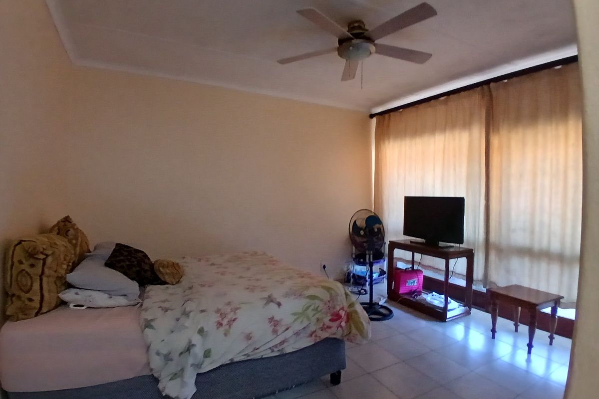 A bedroom featuring tiled flooring, a ceiling fan, and large windows with curtains, providing natural light and a functional living space.