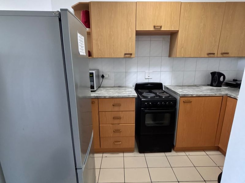 Functional kitchen featuring light wood-tone cabinetry, stone-look laminate countertops, tiled backsplash, and ceramic floor tiles with a freestanding electric stove.