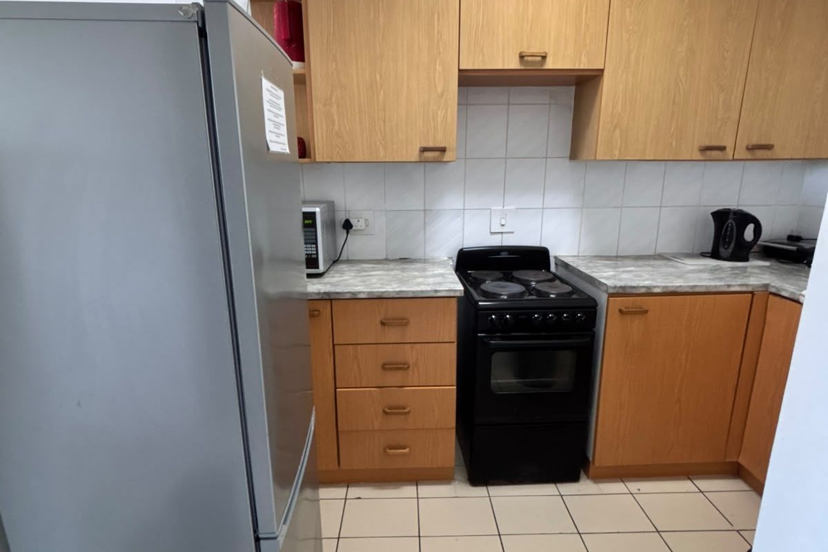 Functional kitchen featuring light wood-tone cabinetry, stone-look laminate countertops, tiled backsplash, and ceramic floor tiles with a freestanding electric stove.