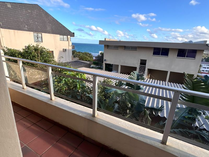 A balcony featuring tiled flooring and a glass balustrade, offering an elevated view of the surrounding neighbourhood and the ocean.