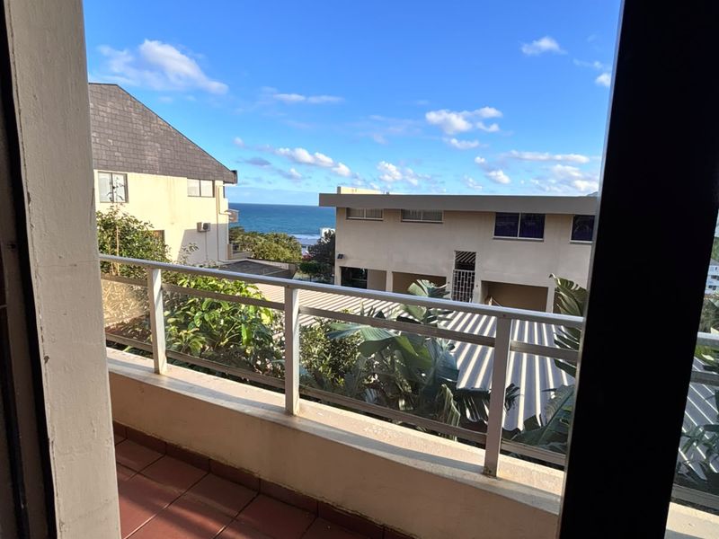 A balcony featuring tiled flooring and a metal balustrade, offering an elevated view of the surrounding neighborhood and the ocean.